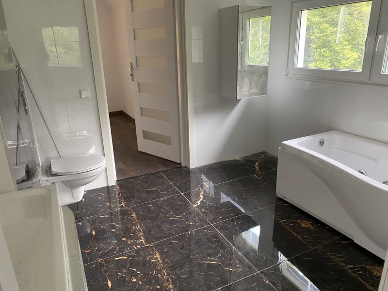 Renoverat badrum med svart marmorklinker med guldådring, vägghängd toalett och bubbelbadkar