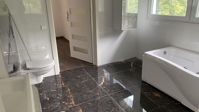 Renoverat badrum med svart marmorklinker med guldådring, vägghängd toalett och bubbelbadkar