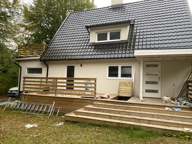 Baksidan av en villa med nytt svart tak, takkupa och nybyggd altan med bred trappa