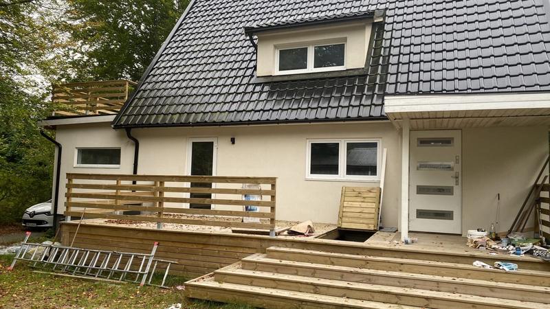 Baksidan av en villa med nytt svart tak, takkupa och nybyggd altan med bred trappa